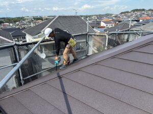 猛暑の屋根上でブロワーを使い雨樋清掃や下地処理を行う塗装職人